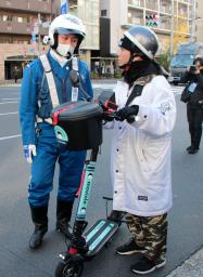 <p>　電動キックボードを運転する男性を呼び止める警視庁の警察官＝１５日午前、東京都港区</p>