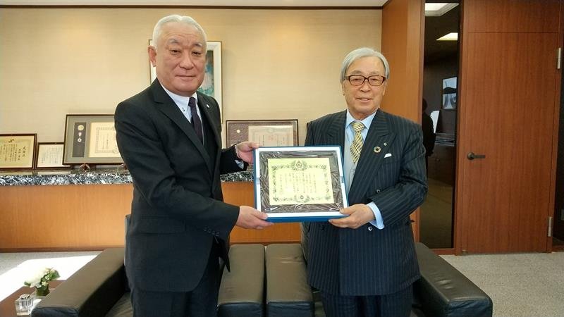 込山事務局長（左）から金色有功章を手渡される金綱会長
