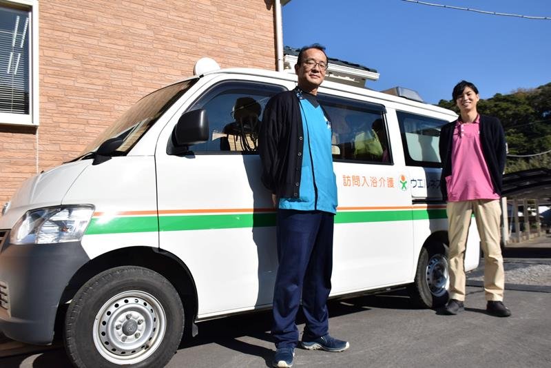 多辺田秀隆社長（左）と常務の貴広さん。後ろは浴槽を積み込んだ入浴車両＝銚子市

