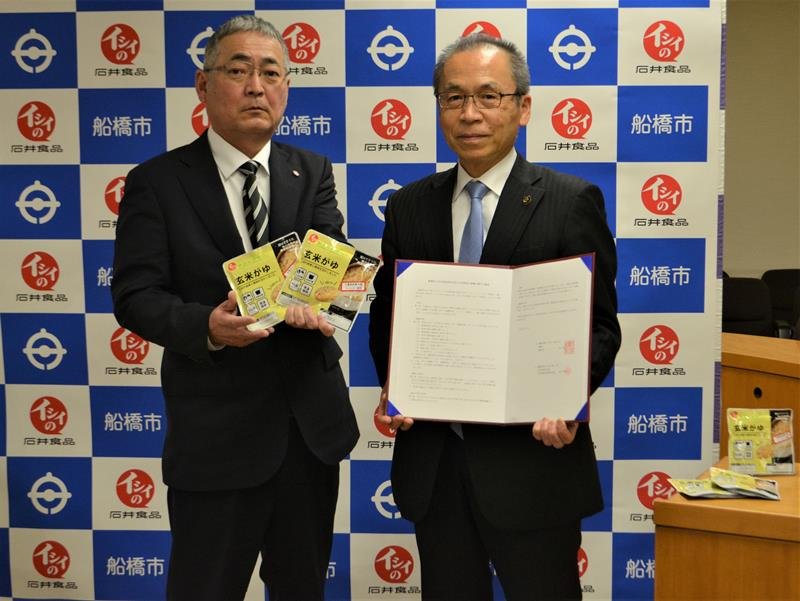 船橋産の米で試作した非常食「玄米がゆ」を手にする石井食品の久保取締役（左）と松戸市長＝７日、船橋市役所
