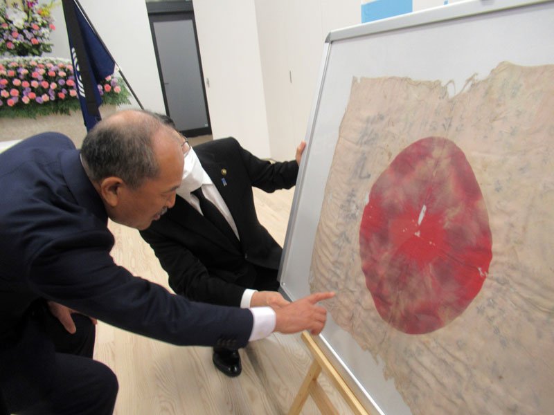 父の日章旗に書き込まれた寄せ書きに見入る松丸裕一さん（左）。右は田中甲市長＝市川市役所