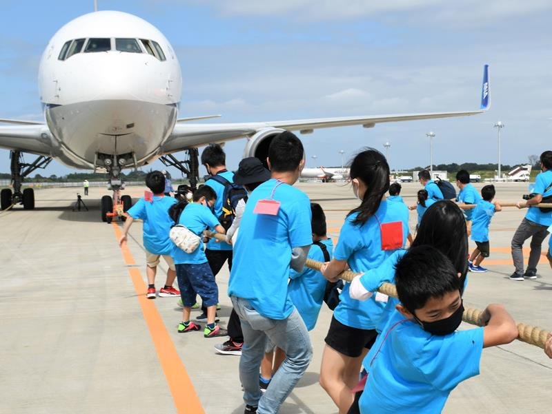 巨大な航空機を一生懸命引っ張る親子＝２５日、成田空港