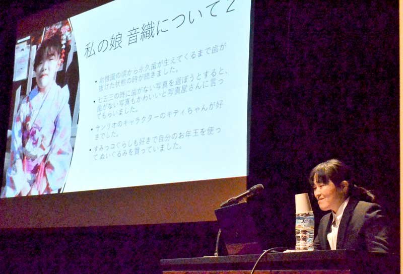 スクリーンに映し出された安藤音織さんの写真の前で講演する母親の正恵さん＝２６日、千葉市中央区