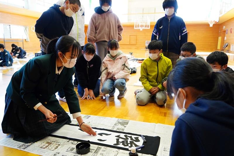 手本を書く高校生のアドバイスに耳を傾ける児童たち＝大多喜町立西小
