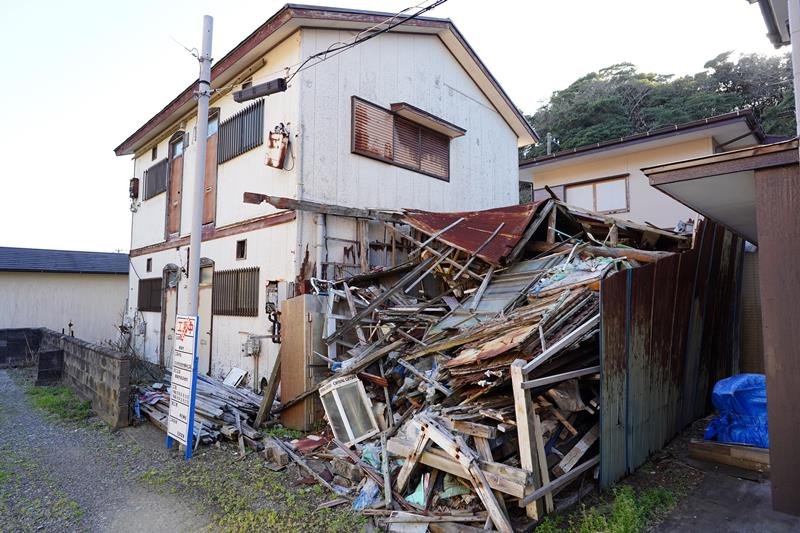 行政代執行による解体作業が始まった特定空き家の木造２階建てアパートと倉庫＝勝浦市串浜
