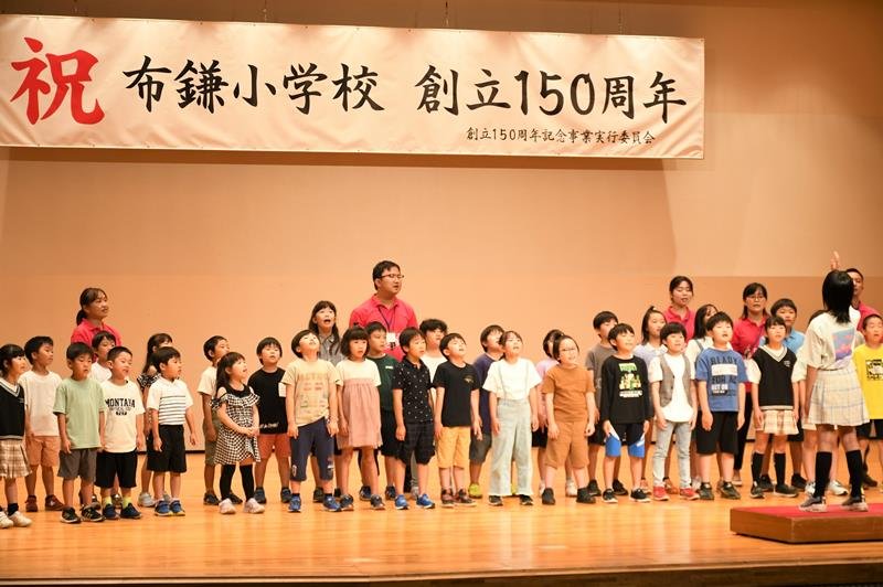 布鎌小の１５０年の歴史を伝える式典で合唱する児童ら＝１７日、栄町
