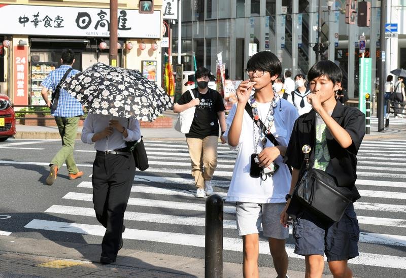 厳しい暑さの中、日傘を差したりアイスを食べたりして交差点を歩く人たち＝１８日午後４時２５分ごろ、千葉市中央区