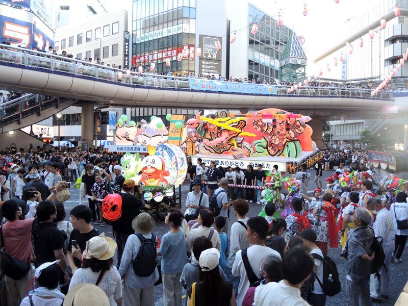 柏駅西口広場で大勢の観衆に囲まれる柏ねぶた。左は「フリースクールゆうび小さな学園」の制作したねぶた＝２９日、柏市