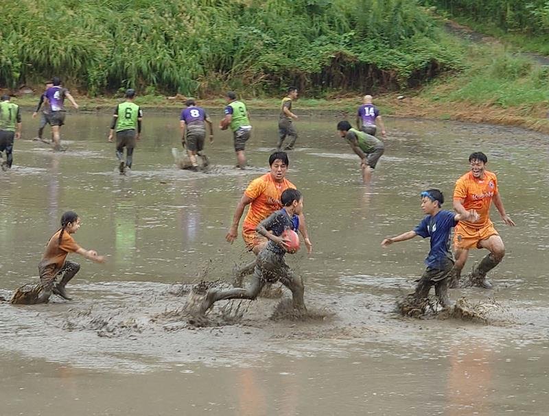 田んぼラグビーで泥まみれになりながら、クボタスピアーズの選手に挑む小学生らのチーム＝２３日、市原