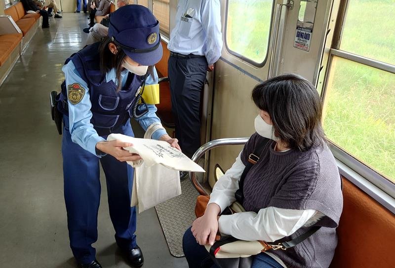 小湊鉄道の車内で、乗客に電話de詐欺への警戒を呼びかけるチラシと防犯グッズを配る市原署員＝１８日、市原市内
