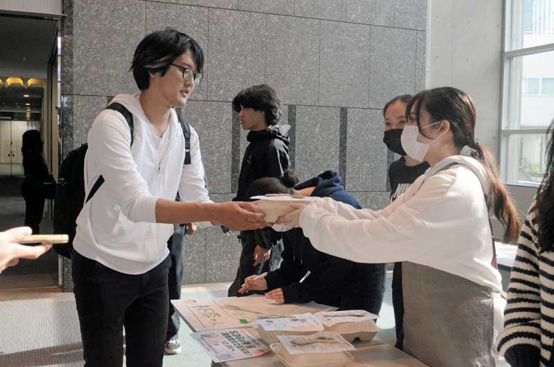 ゼミ生（右）から無料弁当を受け取る学生＝１日、東金市