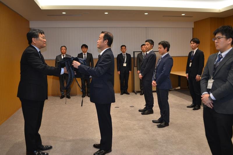 ヘルメットや軍手など被災地支援に必要な物品が入ったリュックを、神谷市長（左）から受け取る市職員＝５日、千葉市役所
