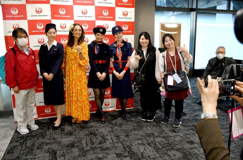 日本初の国際線旅客便就航時に着用された２代目制服姿の客室乗務員（左から２人目）たちと記念撮影するツアー参加者＝成田市の成田空港