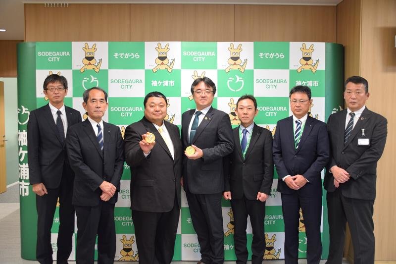 とうもろこしアイスを持つ斎藤社長（左から３人目）と粕谷市長（同４人目）＝袖ケ浦市
