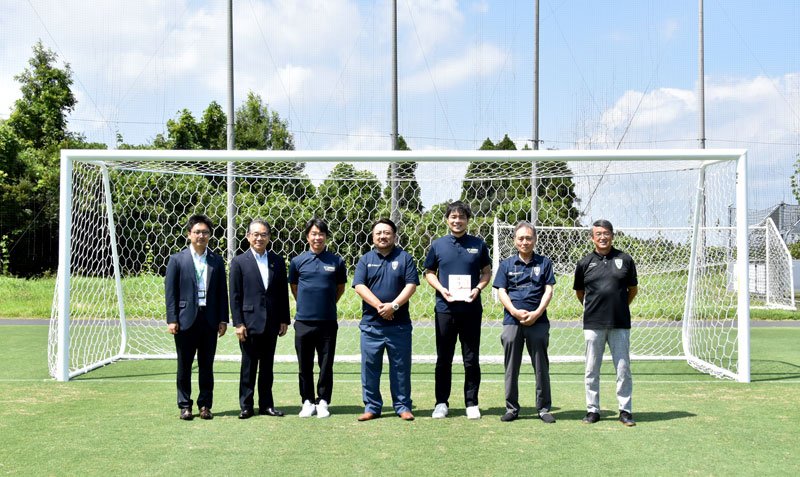 サッカーのゴールを贈った赤坂社長（左から４人目）と目録を持つ佐藤社長（同５人目）＝市原市