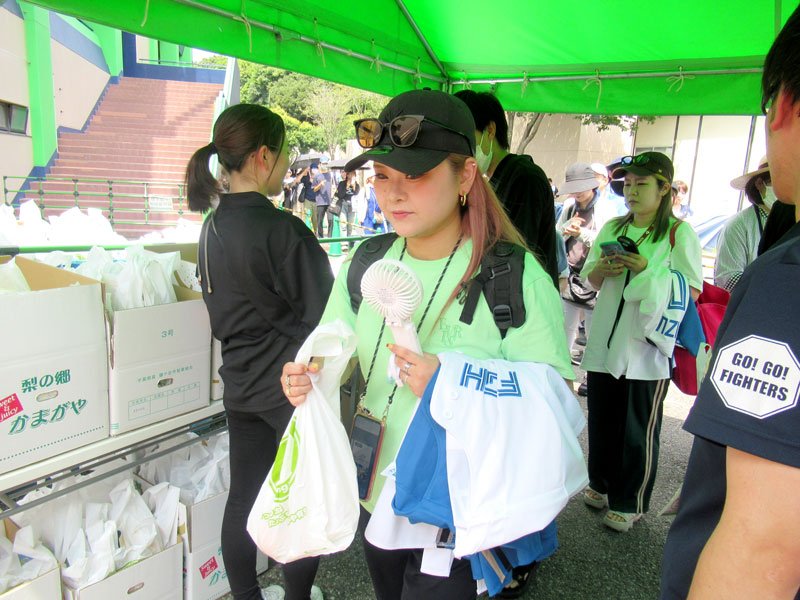梨入りの袋を受け取り球場に入る人たち＝２１日、鎌ケ谷スタジアム