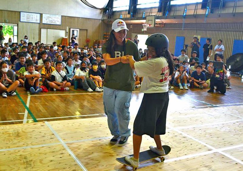 四十住選手（左）に手を握られスケボーを初体験する小学生＝１８日、千葉市中央区