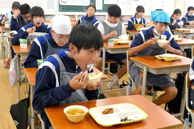 自分たちで生産したコメを頬張る勝浦中２年の生徒＝１日、勝浦市