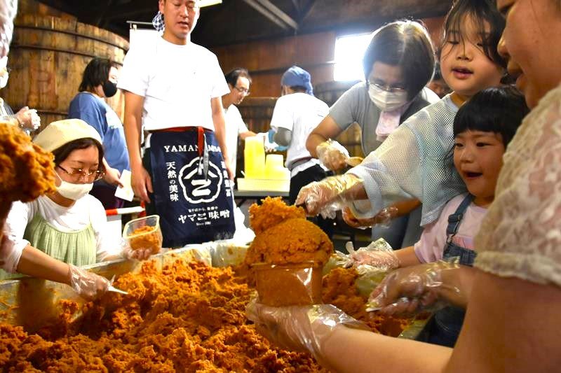 ヤマニ味噌の蔵にある木桶の前で詰め放題に挑戦する来場者＝１９日、佐倉市並木町