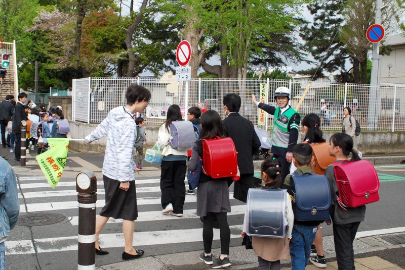 千葉西署員と先生に見守られながら登校する児童たち＝１５日午前７時５０分ごろ、千葉市稲毛区