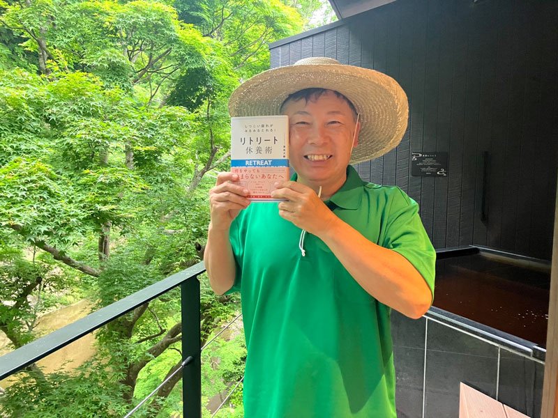 養老渓谷の名所「懸崖境」を背に著書を手にする豊島さん＝５月２９日、大多喜町