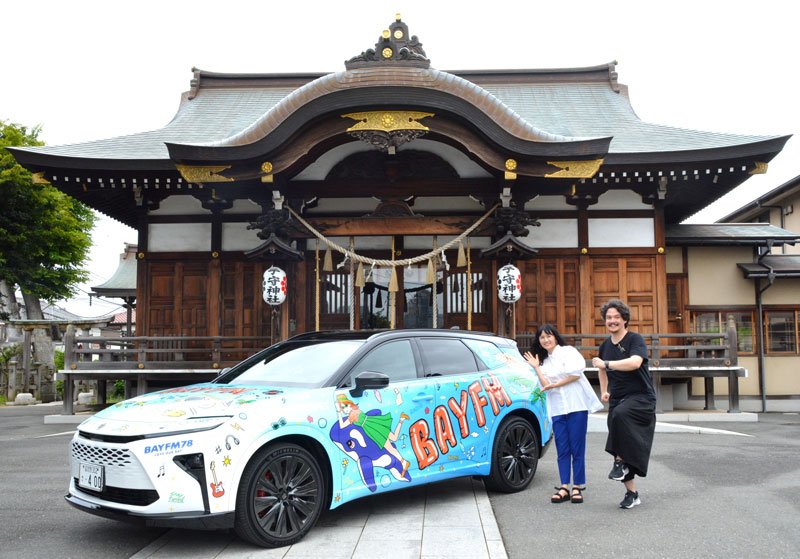 キャンペーンカーの前でポーズを取る（左から）春原さん、フォーンクルックさん＝千葉市花見川区
