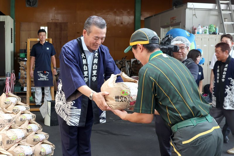 配送業者に返礼品の米袋を手渡す金坂市長（左）＝１８日、大網白里市