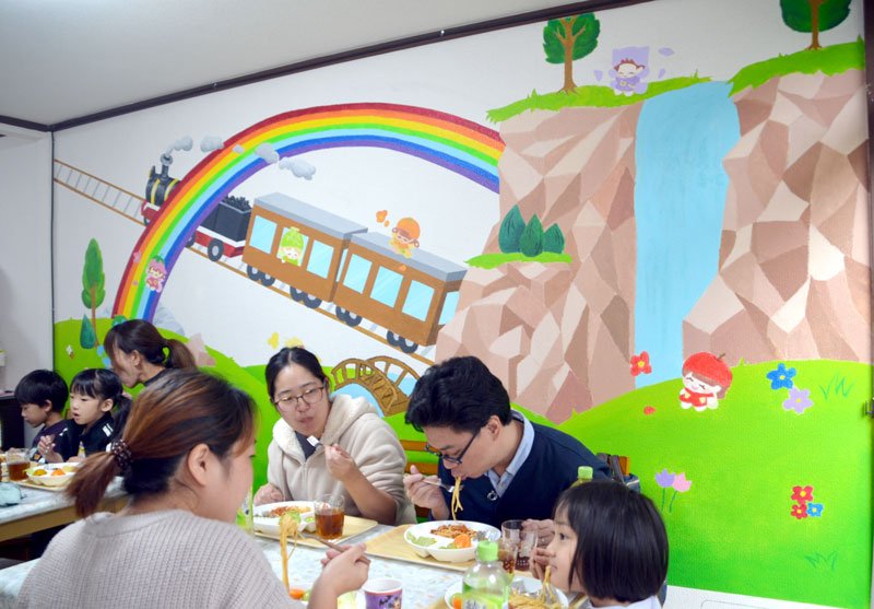 市原八幡高の生徒が描いた壁画の前で食事を楽しむ子どもたち＝２５日、市原市