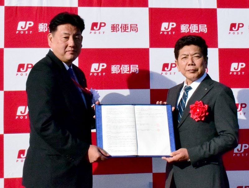 事務の取り扱い開始式で事務受託の契約書を持つ睦沢郵便局の長谷川博一局長（左）と田中町長＝睦沢町