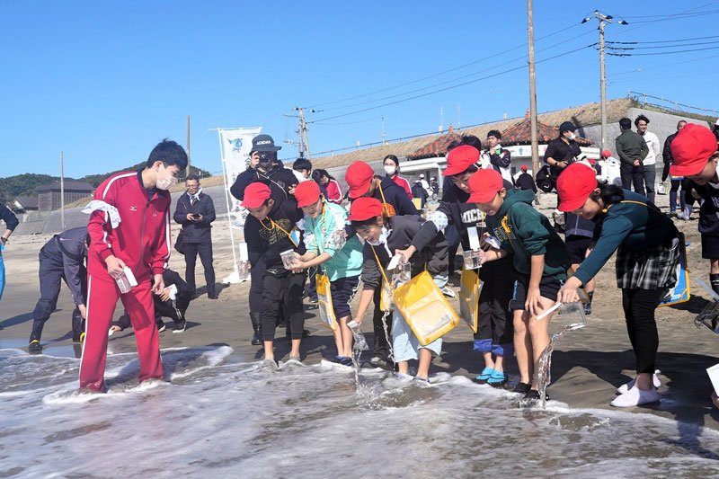 放流体験をする小学生とジャージー姿の長生高校生＝勝浦市
