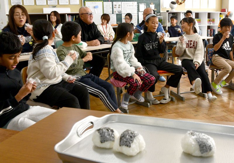 校庭の田んぼで５年生が育てた米で作ったおにぎりを味わう児童ら＝神崎町立米沢小学校