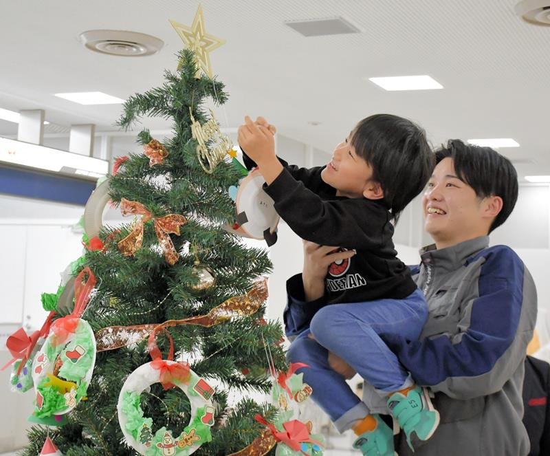 整備士に抱え上げられてクリスマスツリーの高い位置を飾る園児＝成田市