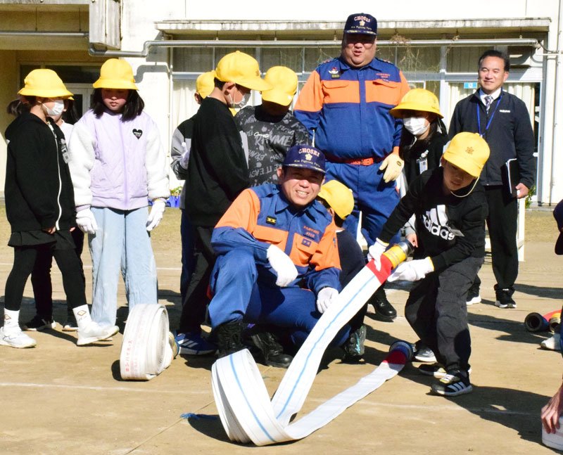 団員に教わりながら、ホースを転がして伸ばす児童＝茂原市立豊岡小