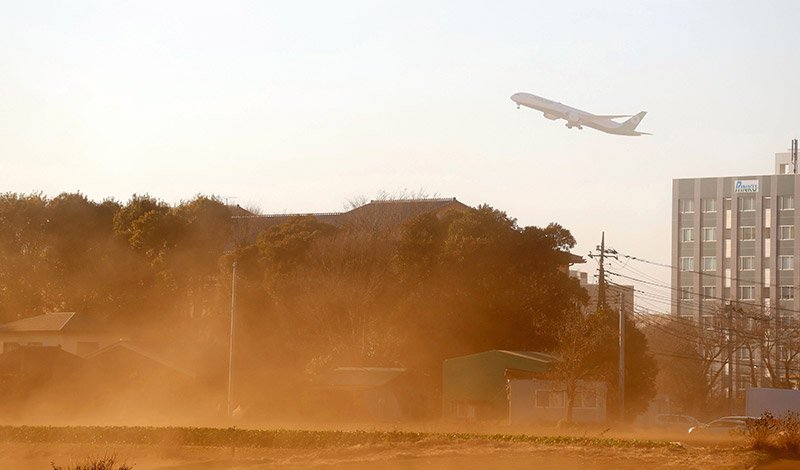 強風の影響で畑の砂ぼこりが舞う成田空港周辺で、上空を飛ぶ離陸機＝１３日午後（芝山町菱田より撮影）