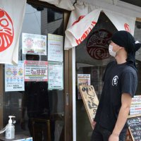 「営業時間短縮のお知らせ」のビラの前に立つ、「もぢょい有限会社」の大将小畑正義さん＝２８日午後、千葉市花見川区
