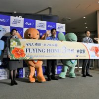 フライングホヌの３号機就航を祝うウミガメのマスコットキャラクターと岡支店長ら（中央）＝２０日夜、成田市の成田空港
