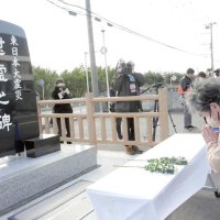 慰霊碑に献花し手を合わせる人たち＝１１日午後２時２７分、いいおかユートピアセンター駐車場